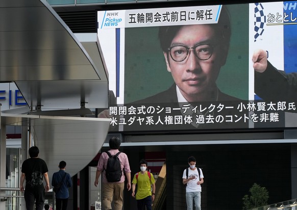 epa09357840 Pedestrians walk past a huge display showing news report about the Tokyo 2020 Organising Committee sacking of Tokyo Olympic Opening Ceremony director Kentaro Kobayashi, in Tokyo, Japan, 22 ...