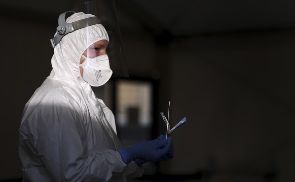 An employee in protective clothing and wearing a nose and mouth mask and face visor holds a swab in her hand at the Covid 19 test centre of the University Hospital in Magdeburg, Germany, Friday, Dec.  ...