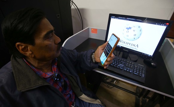 epa10447376 A man looks at a mobile phone next to a laptop showing the blocked internet access to the Wikipedia website, in Karachi, Pakistan, 04 February 2023. A PTA spokesperson said that the Pakist ...