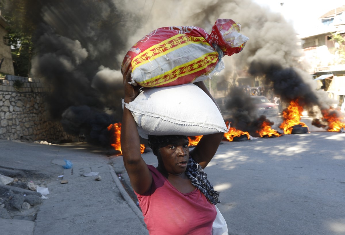 A woman walks past burning tires set on fire by protesters to call attention to the country's insecurity and demanding the resignation of the prime minister, in Port-au-Prince, Haiti, Thursday, J ...