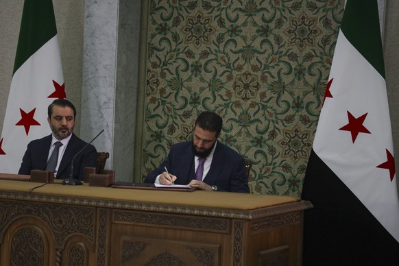 Syria&#039;s interim president Ahmad Al-Sharaa, center, signs a temporary constitution for the country in Damascus, Syria, Thursday March 13, 2025. At left foreign minister Asaad Hassan al-Shiban.(AP  ...