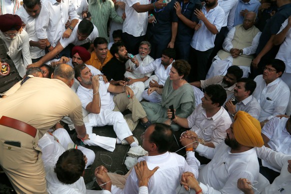 India's opposition Congress party leader Rahul Gandhi drinks water as he participates in a sit-in protest with his sister and lawmaker Priyanka Gandhi Vadra, center right, outside the residence o ...