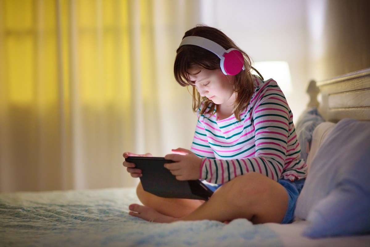 Teenager girl with tablet computer. Teen kid texting and playing online game. School child sending message on social media. Preteen kid in white bedroom doing homework for remote learning. Video chat.