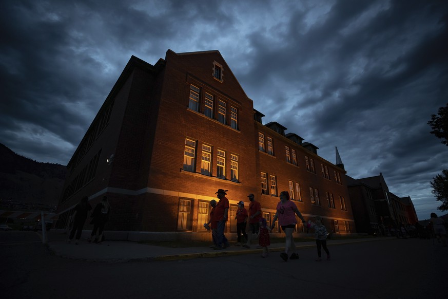 People are silhouetted as they walk past the former Kamloops Indian Residential School after gathering to honor the 215 children whose remains have been discovered buried near the facility, in Kamloop ...