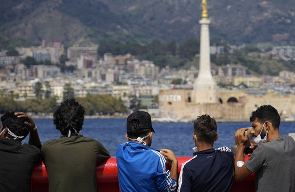 Migrants stand on the deck of the Spanish NGO Open Arms lifeguard ship as they wait to get off the ship after docking at Messina port, in Sicily, Italy, Thursday, Sept. 22, 2022. More than four hundre ...