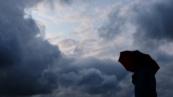 ARCHIV - 12.07.2019, Nordrhein-Westfalen, Duisburg: Ein Mann geht mit einem Regenschirm vor aufziehenden dunklen Wolken spazieren. (zu dpa:
