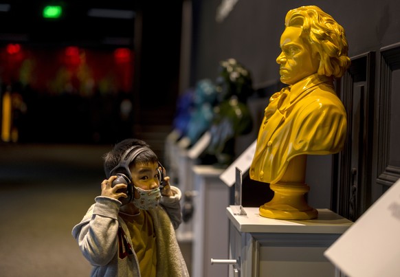 epa09023450 A boy wearing a mask for protection listens with headphones near a Beethoven installation in the Concert Hall in Shanghai, China, 19 February 2021. The Shanghai Concert Hall marked the 250 ...