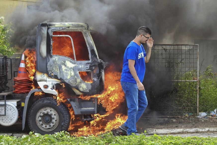epa10522713 A man walks past a burning truck, in Parnamirim, in the state of Rio Grande do Norte, Brazil, 14 March 2023. At least 14 cities in the state of Rio Grande do Norte, in northeastern Brazil, ...