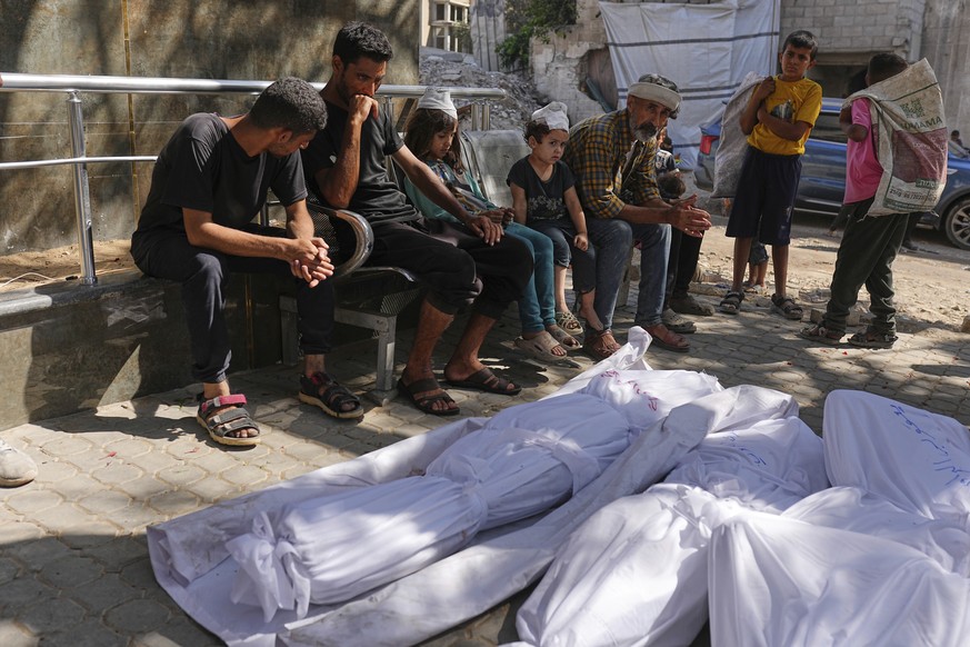 Palestinians sit next to the bodies of their relatives who were killed along with others in an Israeli strike that targeted a school in the northern Gaza Strip, at Shifa Hospital in Gaza City, Friday, ...