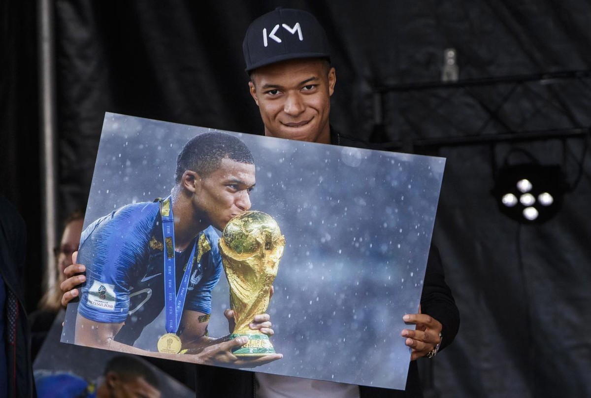 epa07100188 France's soccer player Kylian Mbappe (R) poses with a picture of him kissing the Jules Rimet trophy during his first visit to the Leo Lagrange stadium in his childhood city, since Fra ...