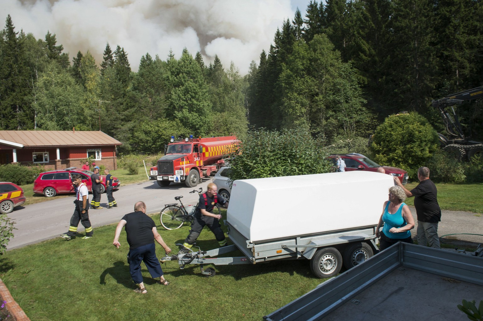 Einwohner eines vom Feuer bedrohten Dorfes und Einsatzkräfte der schwedischen Feuerwehr bereiten die Evakuation vor.