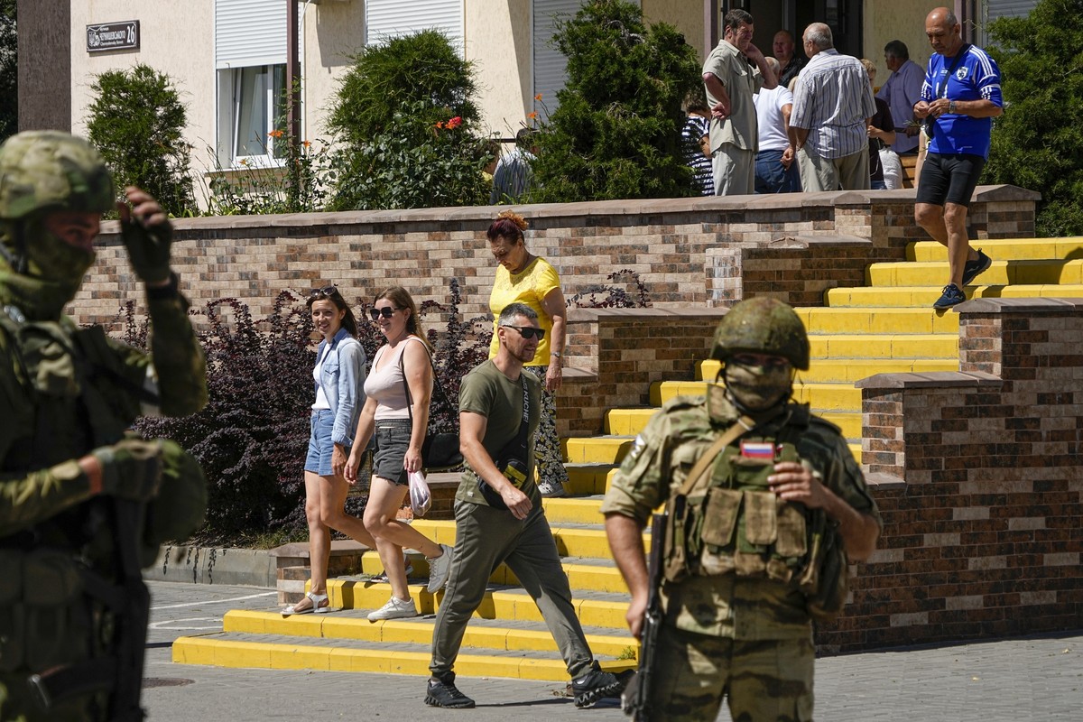 FILE - People walk past as Russian soldiers guard an office for Russian citizenship applications, in Melitopol, south Ukraine, July 14, 2022. Russia took control of part of the Zaporizhzhia region qui ...