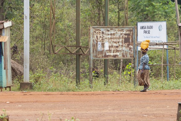 21032026 - Eine Frau traegt einen Sack auf dem Kopf. Im Hintergrund ein verblasstes Schild der Food and Agriculture Organisation der United Nations Genre-Fotos aus Yambio in der Provinz Western Equato ...