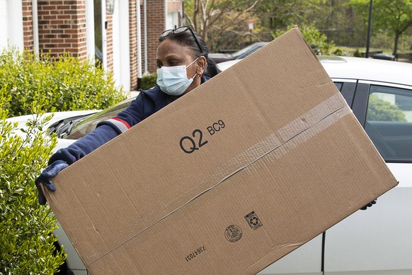 epa08389806 A mail carrier of the United States Postal Service (USPS) wearing a protective face mask delivers a package to a residence in Silver Spring, Maryland, USA, 28 April 2020. US President Dona ...