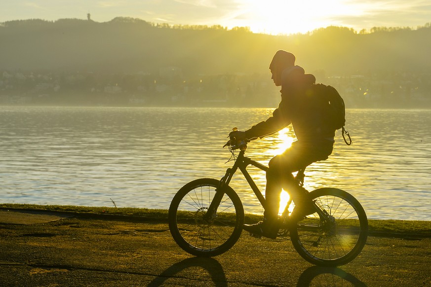 Ein Radfahrer faehrt bei mildem Wetter im goldenen Licht am Ufer des Zuerichsee in Zuerich, am Sonntag, 27. Dezember 2015. (KEYSTONE/Walter Bieri)....A biker rides in the golden light of the sun on th ...