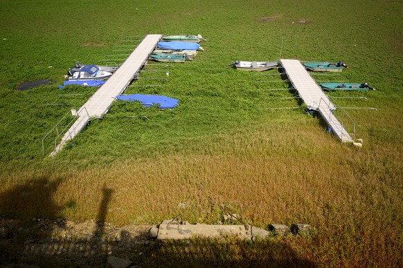 epa10125434 Stranded boats are trapped in mud covered with greenery on the dried out shore of the Lac des Brenets &#039;or Lac de Chaillexon&#039; part of the Doubs river, a natural border beetwen eas ...