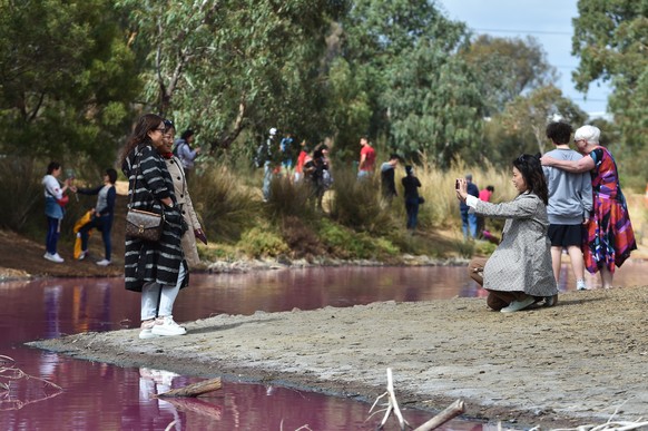 epa07464440 People are seen taking photographs at the Pink lake in Westgate Park, Melbourne, Australia, 26 March 2019. Water in the lake at Westgate park has turned pink due to high salt levels and ha ...