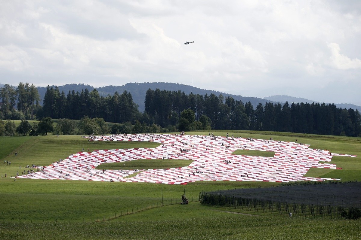 Besucher picknicken auf einem riesigen Picknicktuch, am Sonntag, 11. August 2013 auf dem Ruggisberg bei Roggwil. Das Picknicktuch ist in Kunstprojekt der Kuenstlerzwillinge Frank und Patric Riklin. (K ...