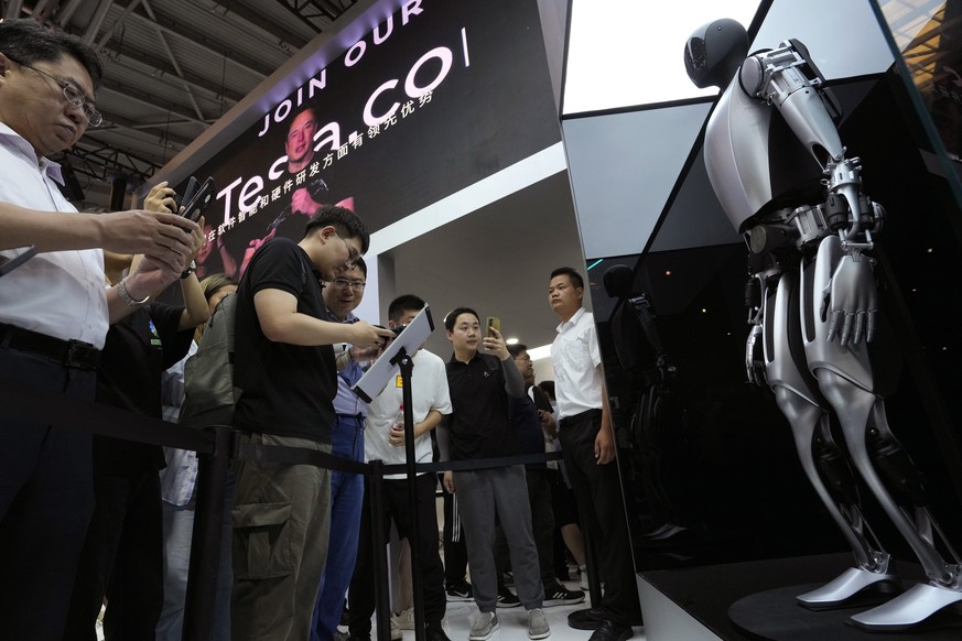 Optimus, also known as Tesla Bot, a robotic humanoid from automaker Tesla, is seen near a screen showing Tesla co-founder and CEO, Elon Musk, top, during the 2023 World Artificial Intelligence Confere ...
