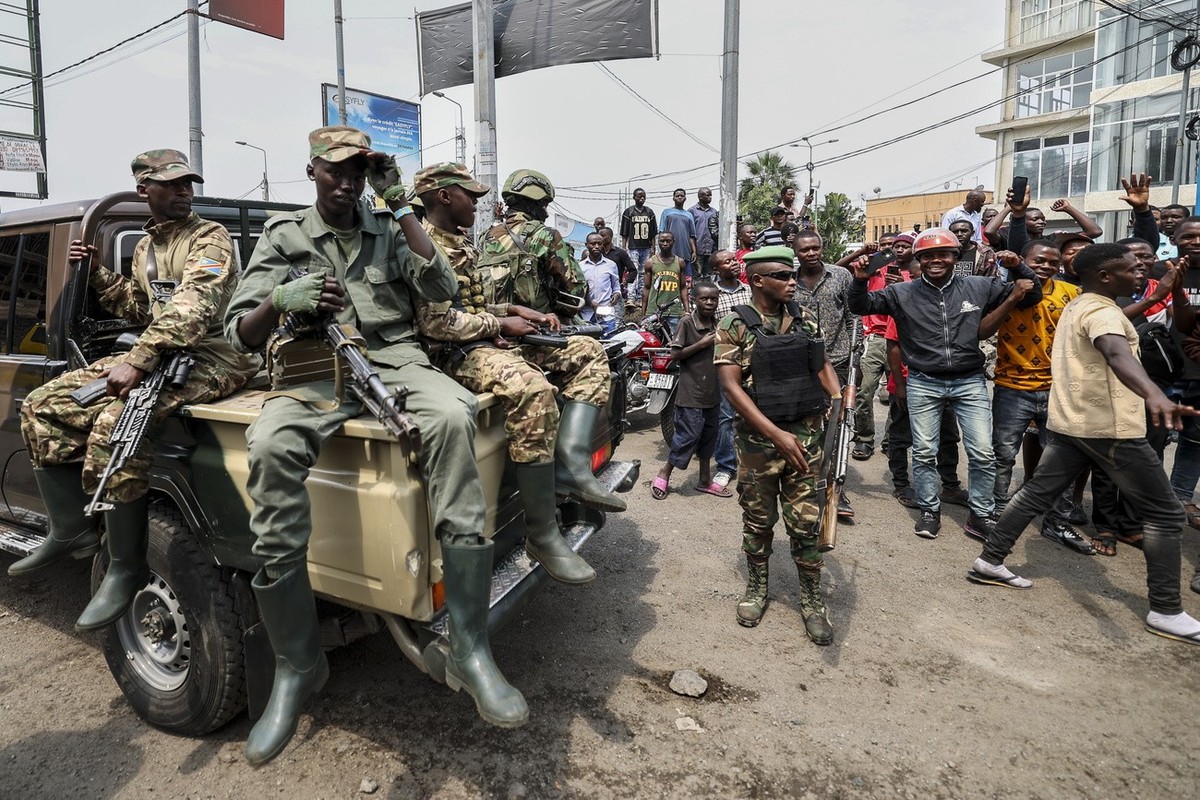 epa11868051 Members of the M23 armed group (L) stand guard along the road sides as they offer security for their leaders, as they arrive to participate in a cleanup exercise of the city of Goma, Democ ...