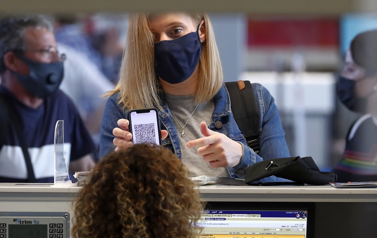 epa09412366 A masked tourist presents her Covid Digital Certificate to a flight desk attendant during a check-in for her flight, at the departures terminal of Henri-Coanda International Airport, in Ot ...