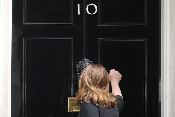 A woman knocks the front door of 10 Downing Street in London, Wednesday, July 6, 2022. A defiant British Prime Minister Boris Johnson is battling to stay in power after his government was rocked by th ...