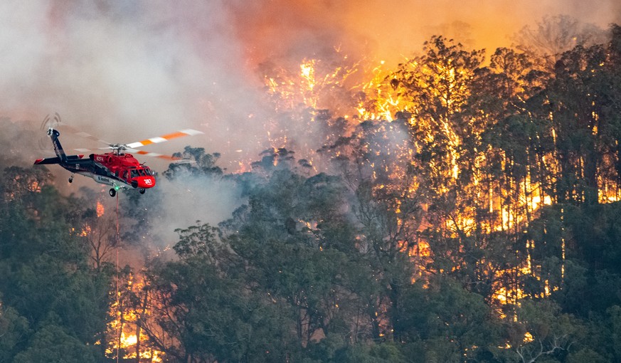 epa08095695 A handout photo made available by the State Government of Victoria on 31 December 2019 shows a firefighting helicopter tackling a bushfire near Bairnsdale in Victoria&#039;s East Gippsland ...