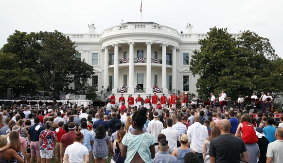 President Donald Trump, accompanied by first lady Melania Trump, places his hand over his heart during the playing of the national anthem during an afternoon picnic for military families on the South  ...