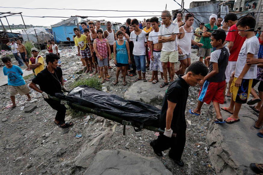 epa05552649 A picture made available on 23 September 2016 shows residents looking on as funeral parlor workers take away the body of an alleged drug user, who was killed during a police operation agai ...