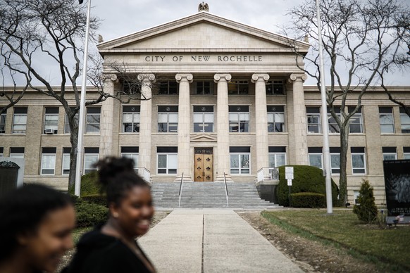 Pedestrians pass New Rochelle City Hall, Tuesday, March 10, 2020, in New York. State officials are shuttering several schools and houses of worship for two weeks in the New York City suburb and sendin ...