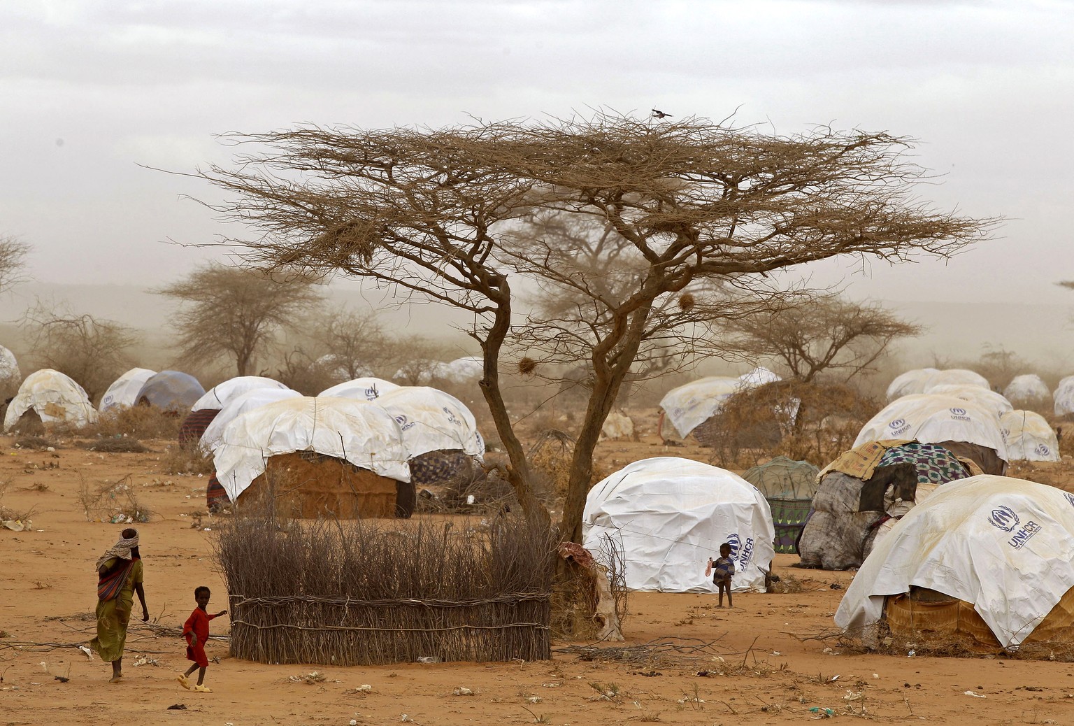 FILE - In this Aug. 4, 2011 file photo, refugees walk amongst huts at a refugee camp in Dadaab, Kenya. Earlier 
in 2017, some Somali refugees whose resettlement in the United States was stopped by Pre ...