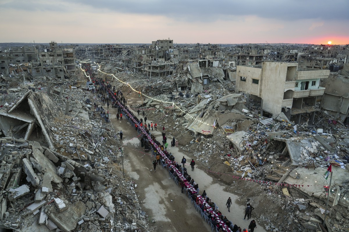 As the sun sets, Palestinians sit at a large table surrounded by the rubble of destroyed homes and buildings as they gather for iftar, the fast-breaking meal, on the first day of Ramadan in Rafah, sou ...