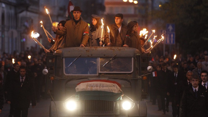 epa05598317 Young people wearing period dresses wave hold torches as they ride an old, historical truck during a march from the Budapest University of Technology and Economics through the streets of B ...