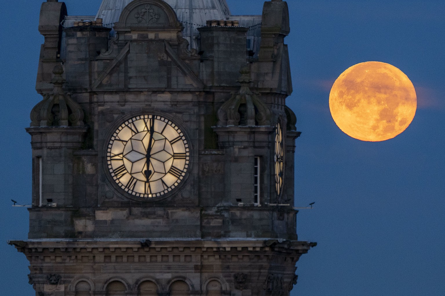 The super blue moon sets behind the Balmoral Clock in Edinburgh Thursday, Aug. 31, 2023. The blue moon refers to the second full moon in one calendar month, which occurs approximately once every two o ...