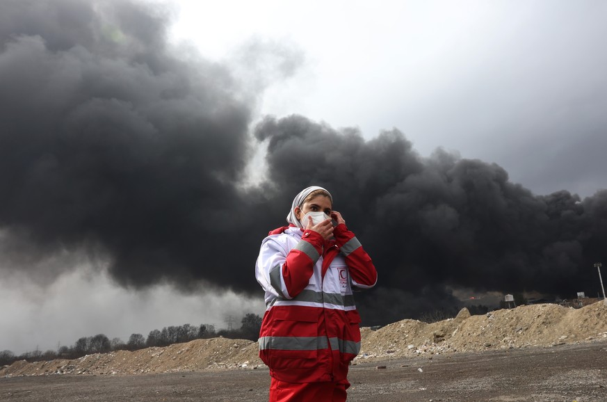 epa12803511 A member of Iran's Red Crescent walks as smoke still rises from Shahran Oil Refinery following last night airstrike in Tehran, Iran, 08 March 2026. A joint Israeli and US military ope ...