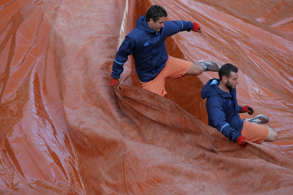 Stadium employees set up a protective canvas on the court as Timea Bacsinszky of Switzerland plays France's Kristina Mladenovic during their quarterfinal match of the French Open tennis tournamen ...
