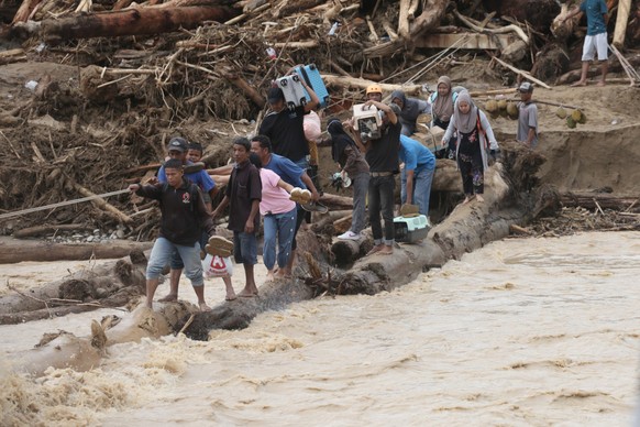Flood survivors use logs to cross a river in Batang Toru, North Sumatra, Indonesia, Tuesday, Dec. 2, 2025. (AP Photo/Binsar Bakkara)