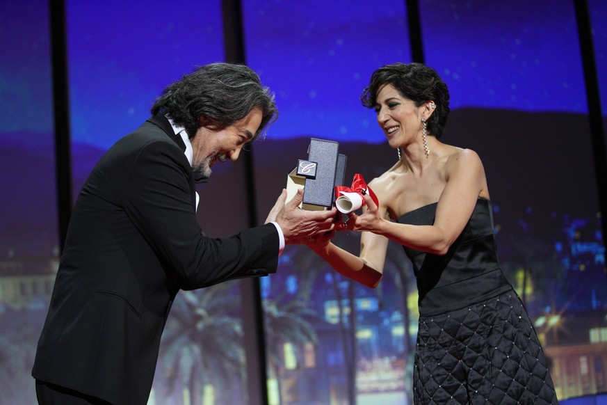 Zahra Amir Ebrahimi, right, presents Koji Yakusho with the Best Actor Award for 'Perfect Days' at the awards ceremony of the 76th International Film Festival, Cannes, South of France, Sa...