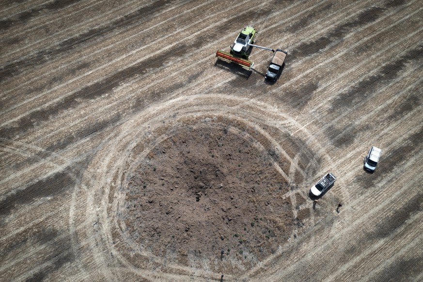 FILE - A farmer collects harvest on a field ten kilometers from the front line, a crater left by the Russian rocket in the foreground, in the Dnipropetrovsk region, Ukraine, July 4, 2022. Warning of a ...