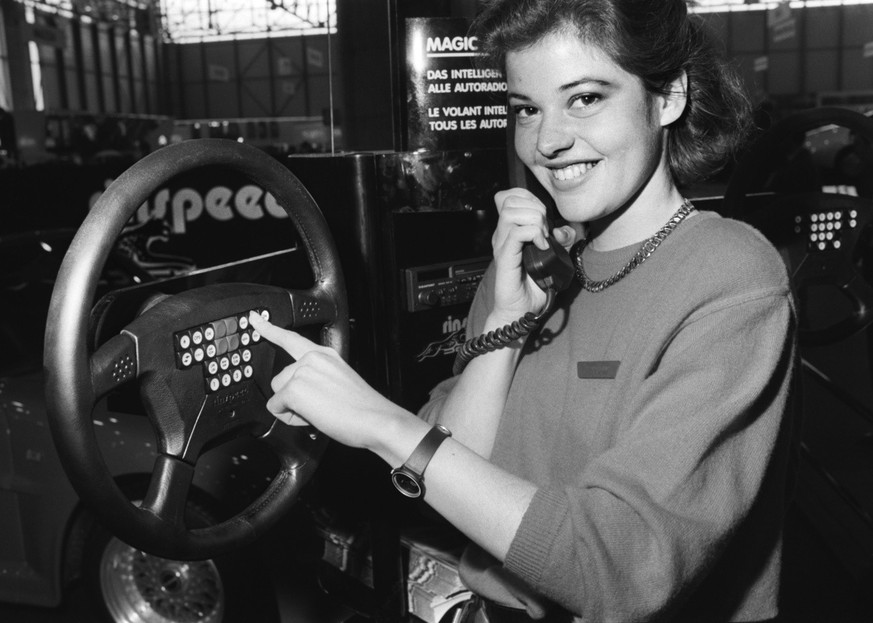 A woman uses a car phone with a keypad integrated into the steering wheel during the 57th Geneva International Motor Show, taken on March 5, 1987. (KEYSTONE/Str)=== === : FILM]