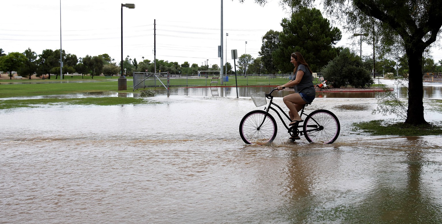 Eine Frau fährt mit dem Velo auf einem überschwemmten Radweg bei der Wüstenstadt Phoenix.