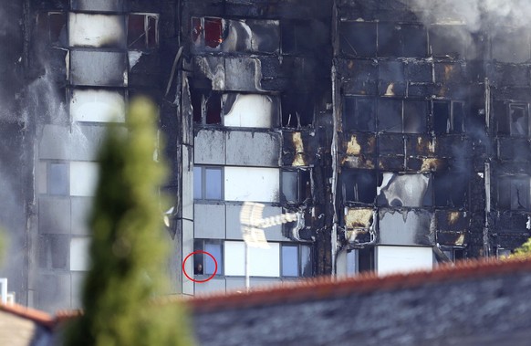 Bild mit rotem Kreis. A man looks from a window of a building on fire in London, Wednesday, June 14, 2017. A massive fire raced through the 27-story high-rise apartment building in west London early W ...