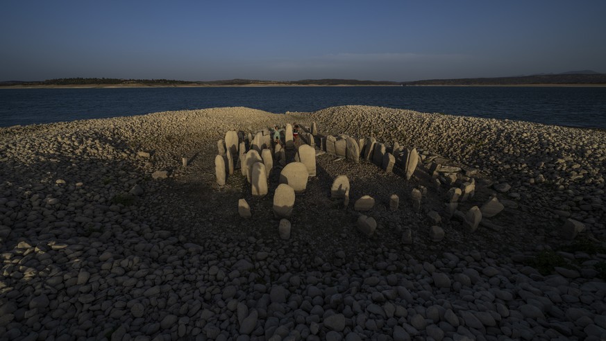 Amalie Garcia, 54, stands next to The Dolmen of Guadalperal, a megalithic monument that emerged due to drought at the Valdecanas reservoir in El Gordo, western Spain, Saturday, Aug. 13, 2022. In the w ...