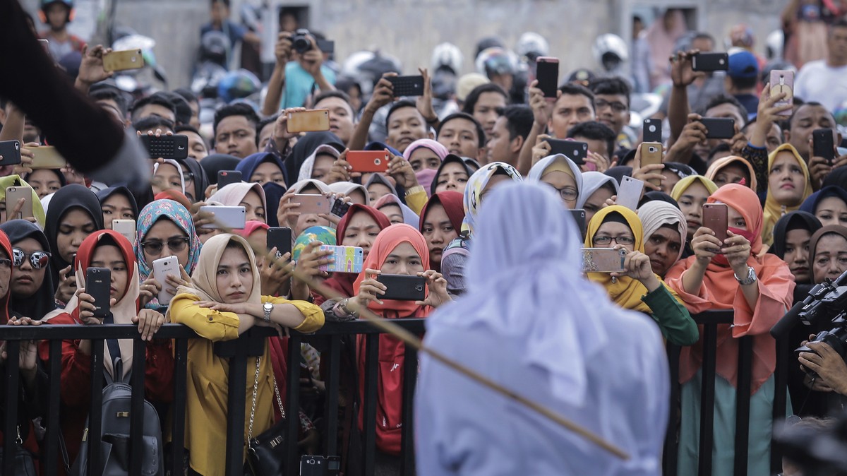 People use their mobile phones to take pictures as a Shariah law official whips a woman who is convicted of prostitution during a public caning outside a mosque in Banda Aceh, Indonesia, Friday, April ...