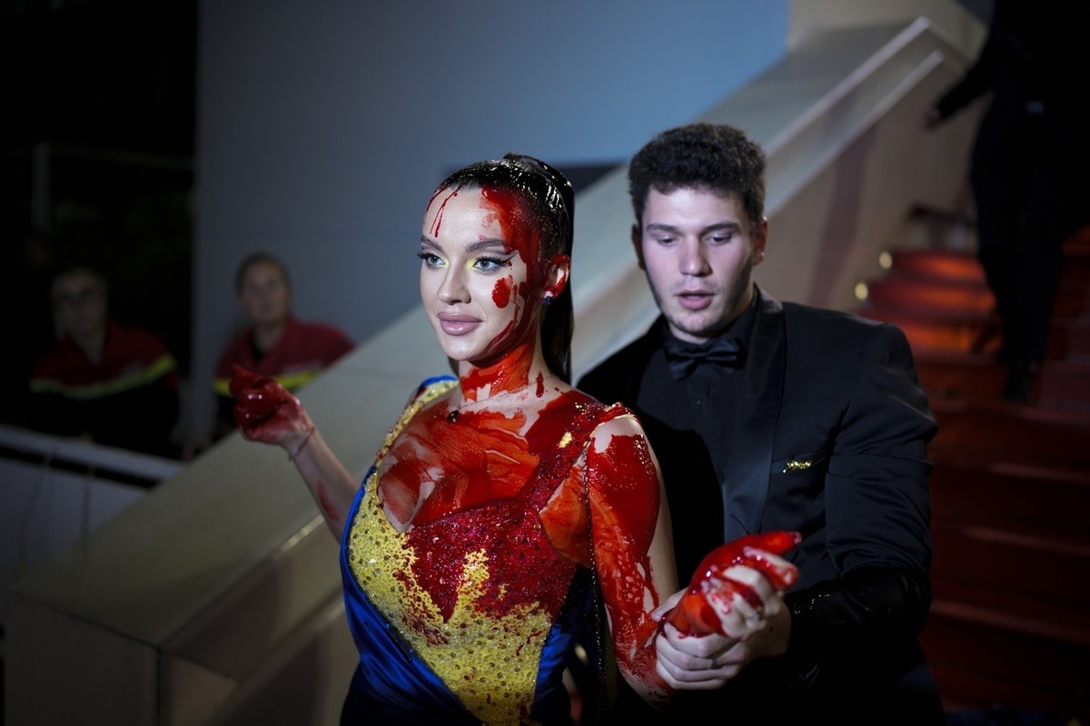 A person, in Ukrainian colours, smeared in a red substance is removed by security at the premiere of the film 'Acide' at the 76th international film festival, Cannes, southern France, Sunday ...