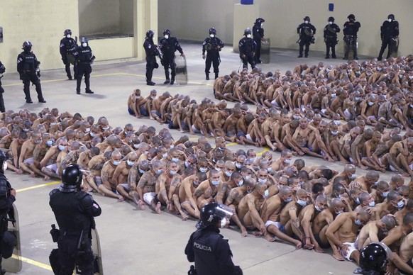 In this photo released by El Salvador Presidency Press Office police wearing masks as precautions against the new coronavirus guard inmates, also wearing masks, during a security operation after Presi ...