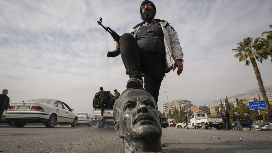 An opposition fighter steps on a broken bust of the late Syrian President Hafez Assad in Damascus, Syria, Sunday Dec. 8, 2024. (AP Photo/Hussein Malla)