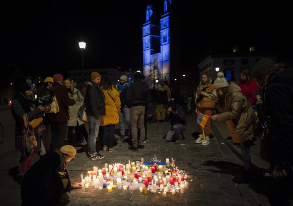 epa09792591 A woman lights a candle as the Grossmuenster church is lit in the colors of the Ukrainian flag during a demonstration against the Russian invasion of Ukraine, in Zurich, Switzerland, 28 Fe ...