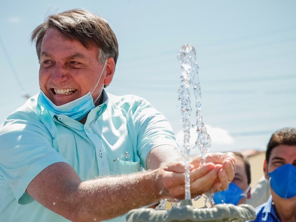 HANDOUT - Auf diesem vom brasilianischen Präsidentenamt zur Verfügung gestellten Bild lächelt Jair Bolsonaro, Präsident von Brasilien, mit untergezogenem Mundschutz, während er an einem Brunnen zur lokalen Wasserversorgung mit Wasser spielt. Foto: Alan Santos/Palacio Planalto/dpa