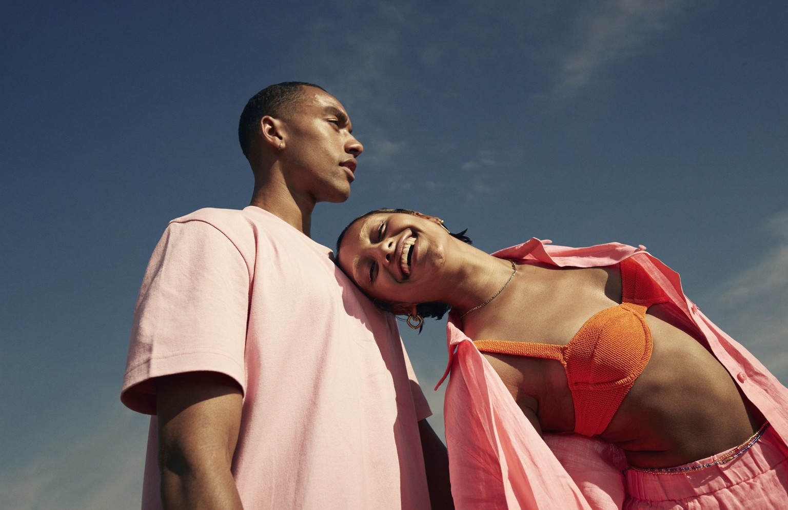 Carefree young woman leaning on male friend while standing against sky